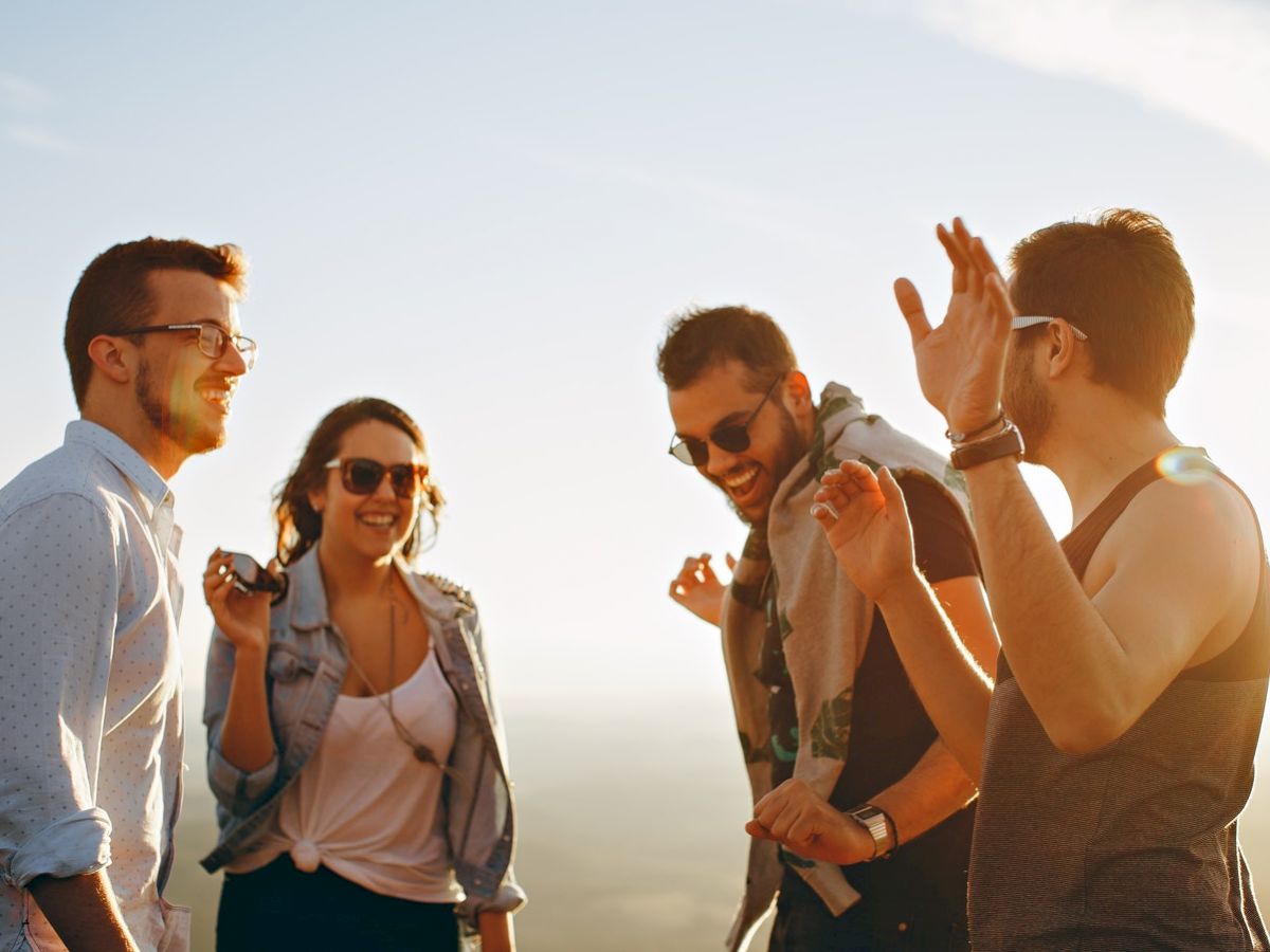 A group of four people laughing and enjoying each other's company outdoors during a sunny day.