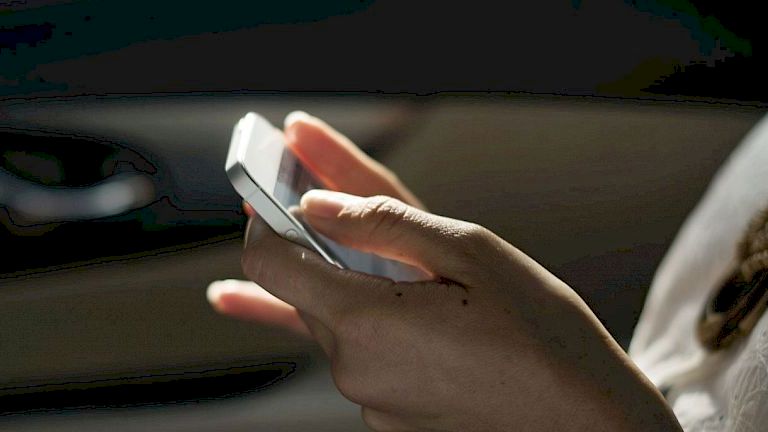 A person holding a smartphone, possibly using or dialing it, inside a vehicle. Only the hand and part of the body are visible in the image.