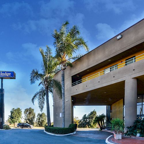 The image shows the exterior of a Travelodge hotel with palm trees, a blue sky, and a parking lot in the foreground, giving a welcoming impression.