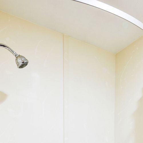 The image shows a shower area with a wall-mounted showerhead and a curved shower curtain rod with a white curtain.