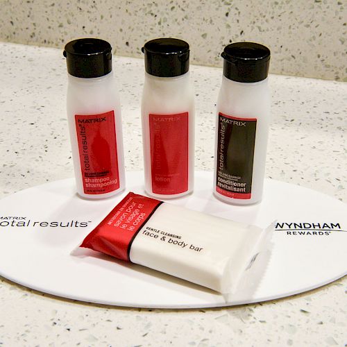 The image shows three small bottles of toiletries and a soap bar on a white tray with “Wyndham Rewards” and “Total Results” branding.