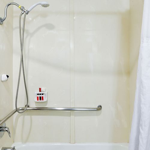 The image shows a white bathtub with a shower head, grab bars, a shower curtain, and a wall-mounted soap dispenser.