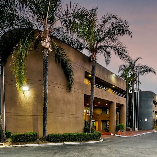 A modern building with palm trees at dusk, featuring clean architecture and a well-maintained landscape, likely an office or hotel.