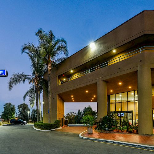 The image shows the exterior of a Travelodge hotel during the evening, with palm trees and lights illuminating the entrance.