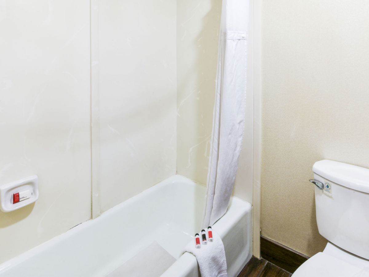 A clean bathroom with a bathtub, white shower curtain, towels, red toiletries, and a white toilet beside the tub, on a wooden floor ending the sentence.