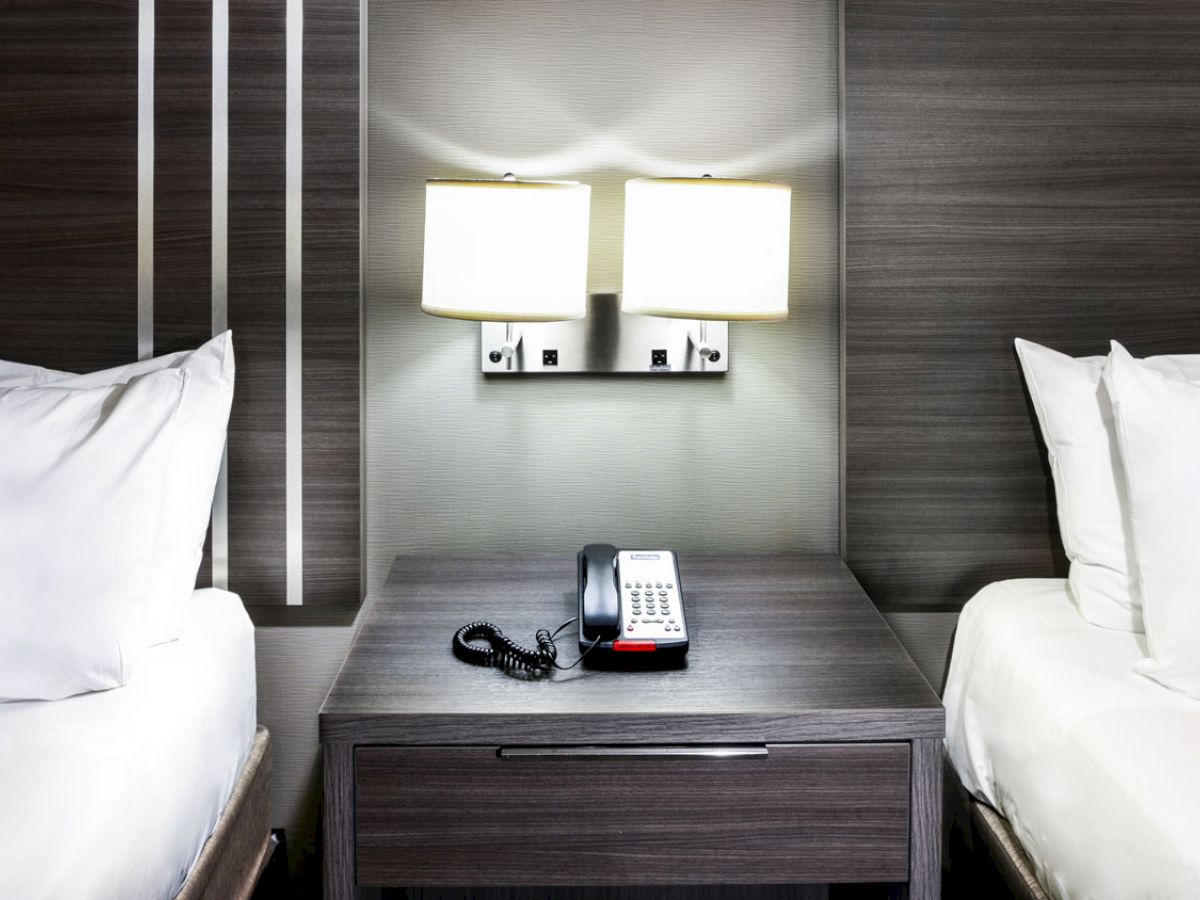 A hotel room with two beds, a nightstand, a phone, and wall-mounted lamps situated between the beds, with clean, modern decor.