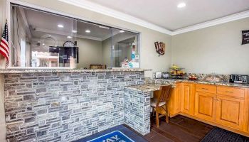 The image shows a reception area with a stone-front desk, a small flag, and a wooden cabinet with fruit and appliances. There's a window to another room.