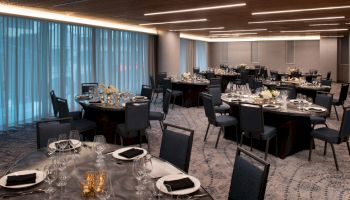 A banquet hall with round tables and chairs, set with plates, glasses, napkins, and centerpieces, under modern lighting.
