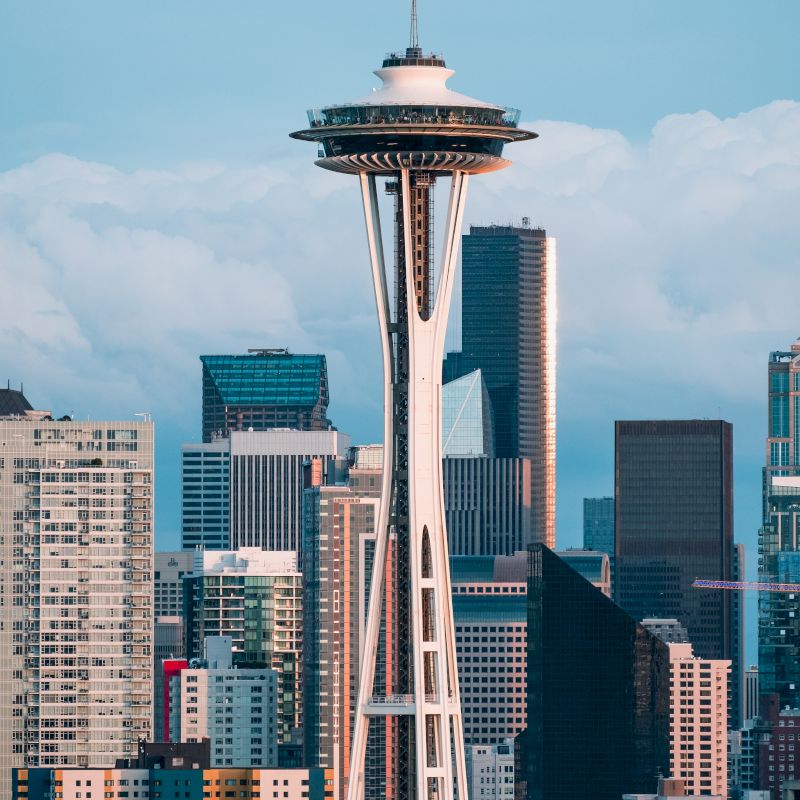 The image shows the Seattle skyline featuring the iconic Space Needle among other skyscrapers, with a backdrop of cloudy skies.