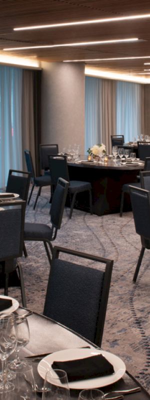 The image shows an elegantly set dining room with several round tables, each adorned with black napkins, wine glasses, and floral centerpieces.