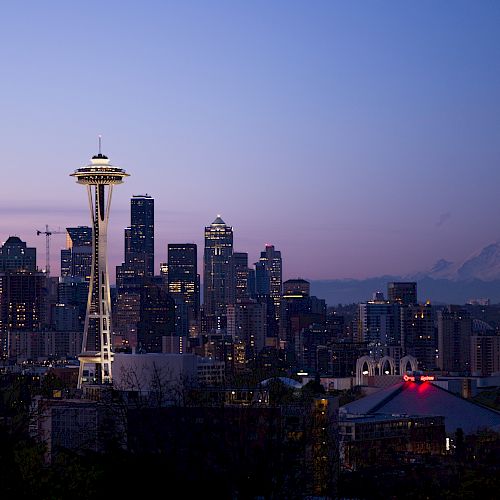 This image shows the Seattle skyline at dusk, featuring the Space Needle and various buildings with Mount Rainier visible in the distance.