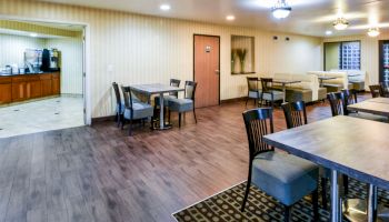 A dining area with multiple tables and chairs, and a door leading to another room with a beverage station visible.